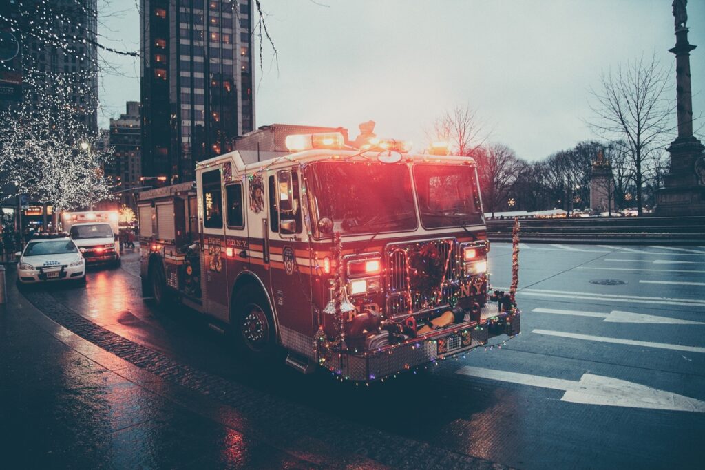 A firetruck adorned with Christmas lights navigates a street.